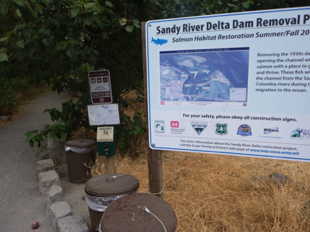 Signage describing salmon habitat restoration with trash cans and park rules